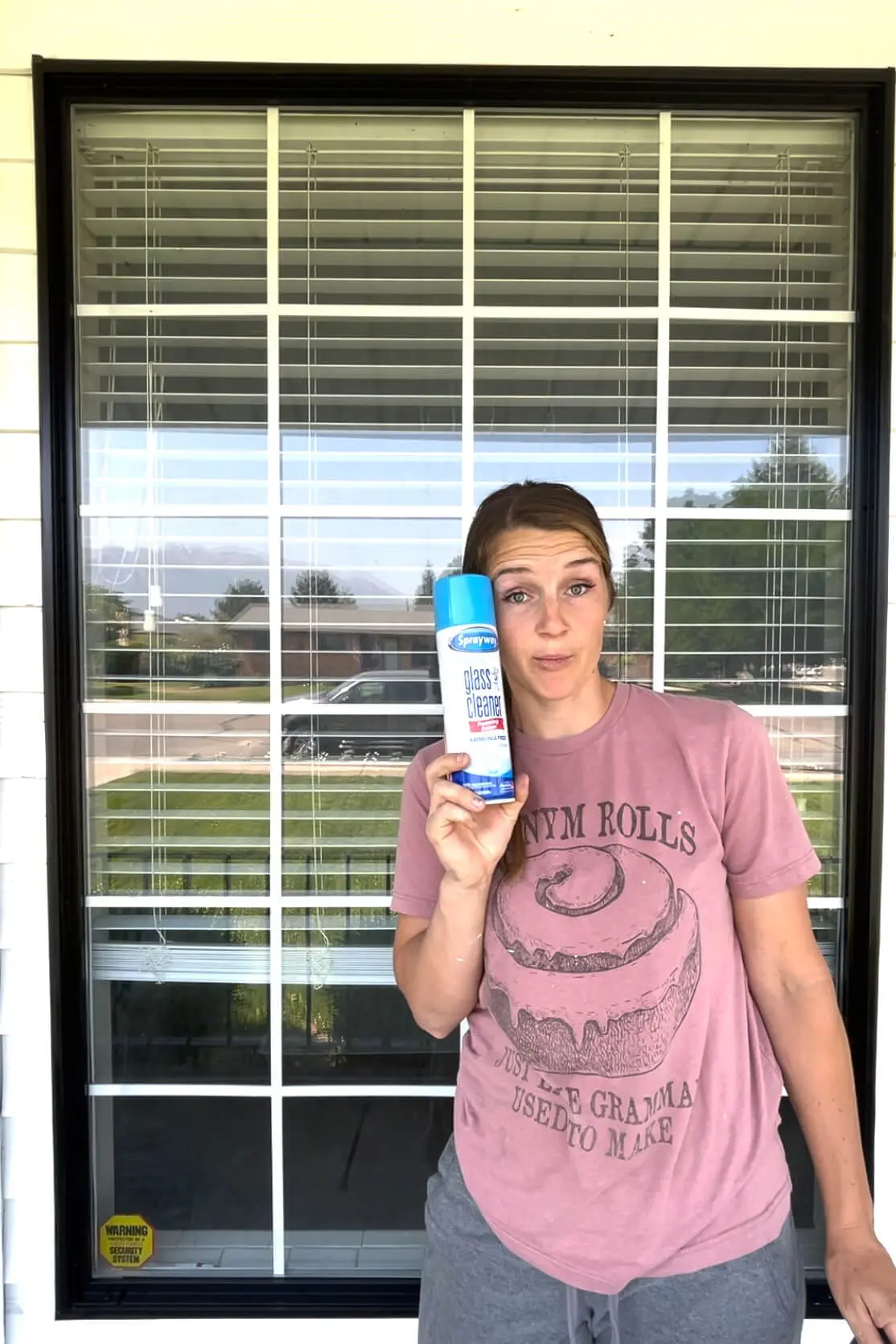 Woman holding a can of Sprayway glass cleaner in front of a freshly cleaned window.